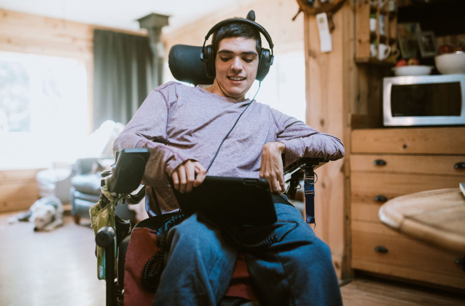 Smiling young man with physical disabilities using a tablet and headphones sitting in a specialized wheelchair