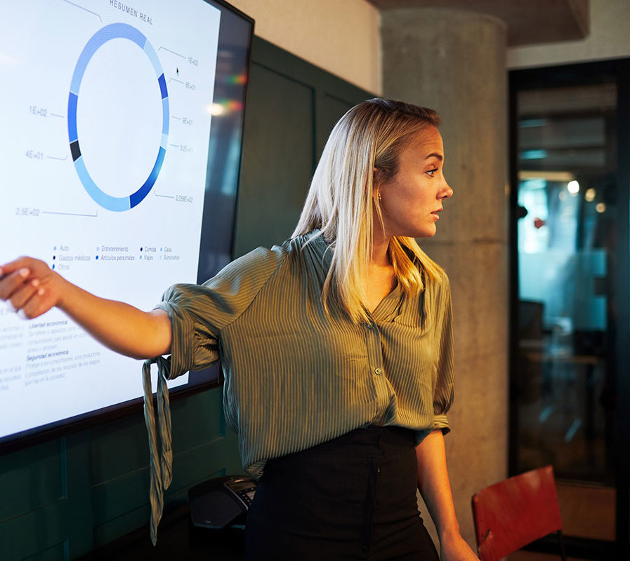 Woman in business attire gesturing at screen showing charts