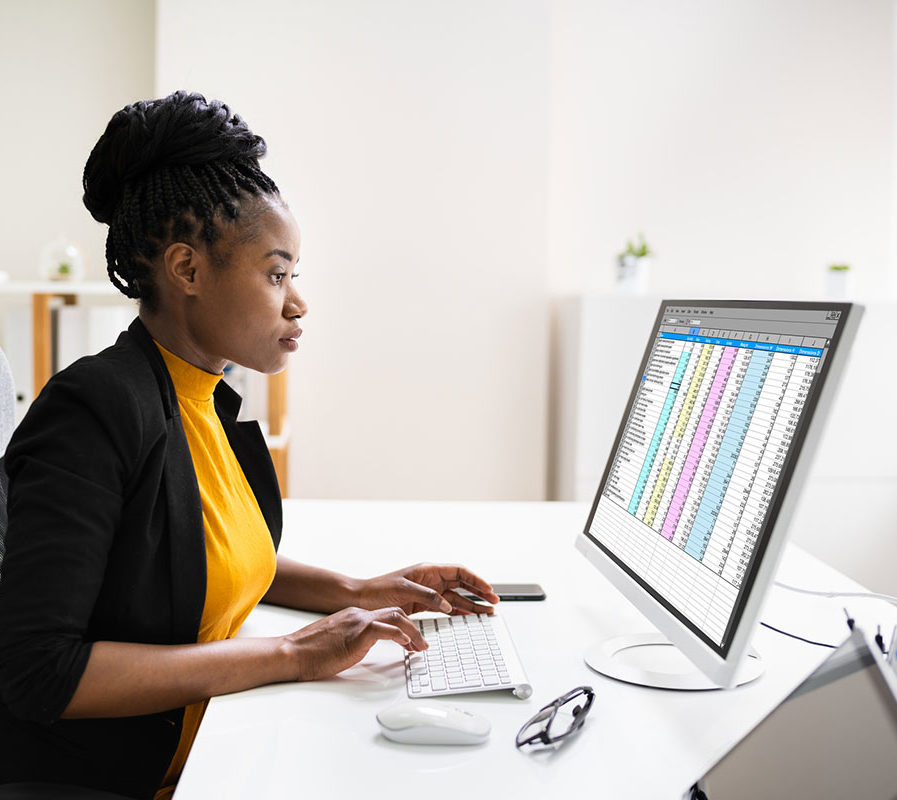 Woman of colour working at a desk in an office with a spreadsheet on the monitor
