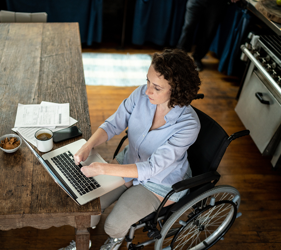 A woman in a wheelchair lacking fingers working on a laptop with a coffee nearby