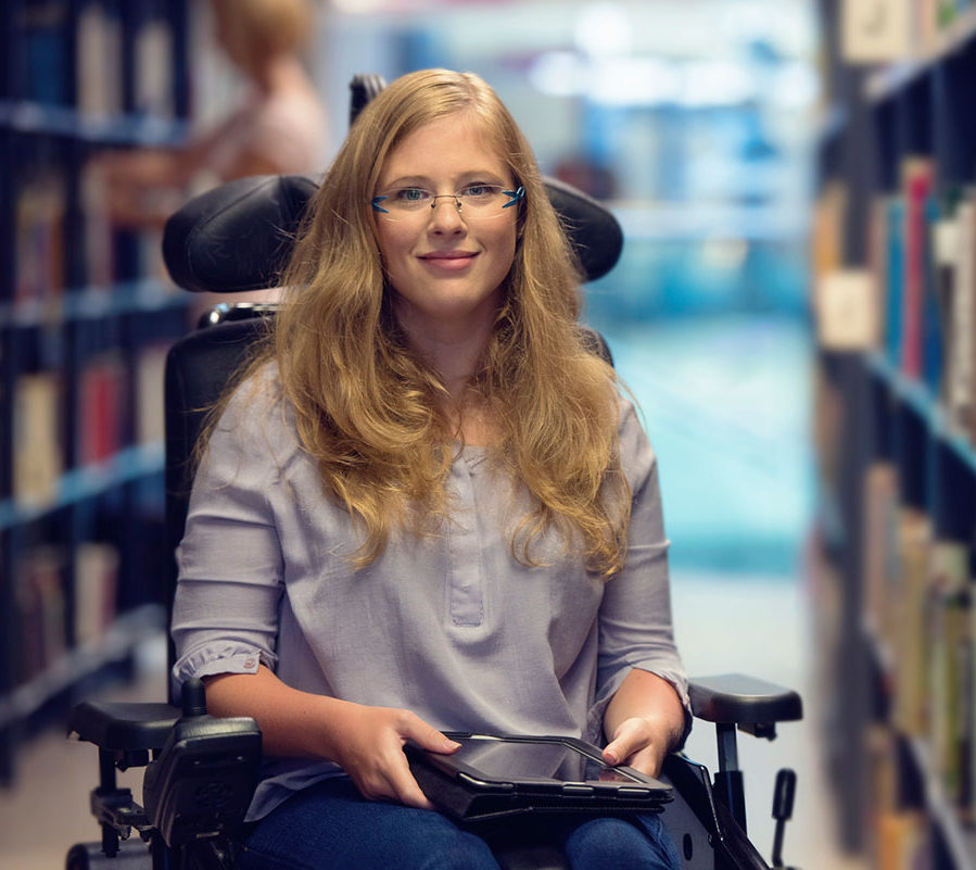 Woman in a wheelchair with a tablet, surrounded by shelves of books
