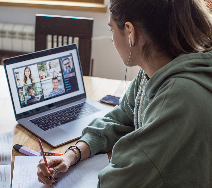 Female student sitting in front of laptop with video conference, holding a pen and surrounded by textbooks